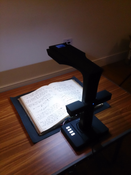 Photo of a book scanner positioned over an open book with hand-written text