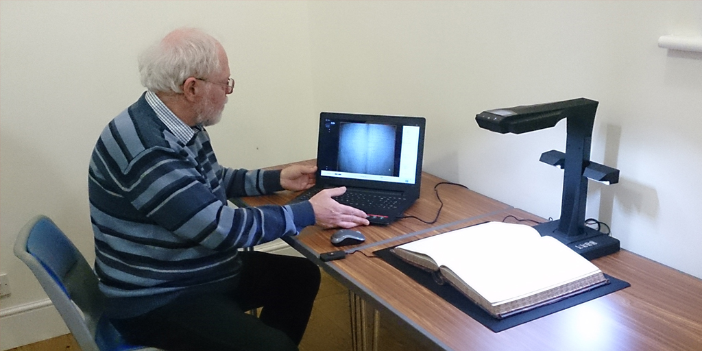 Photo of a man using a laptop computer to together with a book scanner