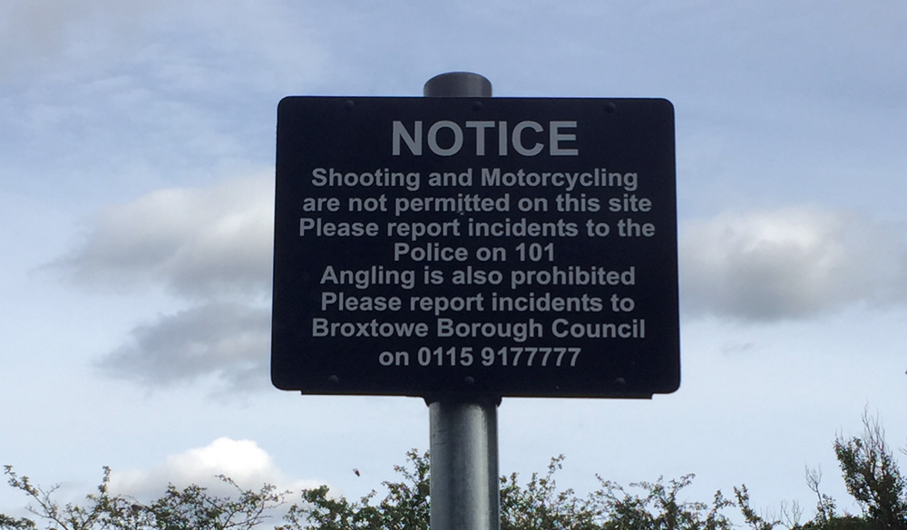 Photo of sign reading "Notice - shooting and motorcycling are not permitted on this site. Please report incidents to the Police on 101. Angling is also prohibited. Please report incidents to Broxtowe Borough Council on 0115 9177777"